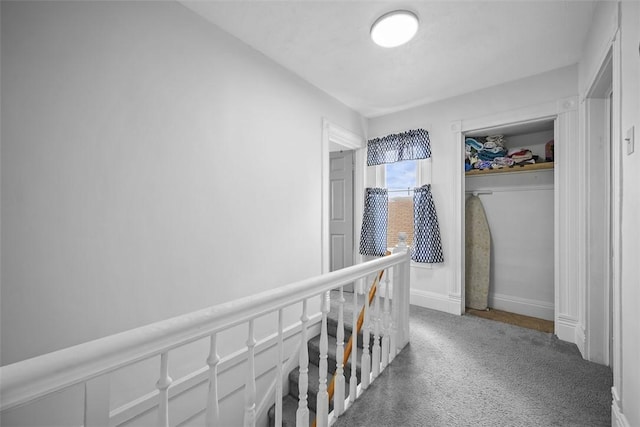 hallway featuring baseboards, carpet flooring, and an upstairs landing