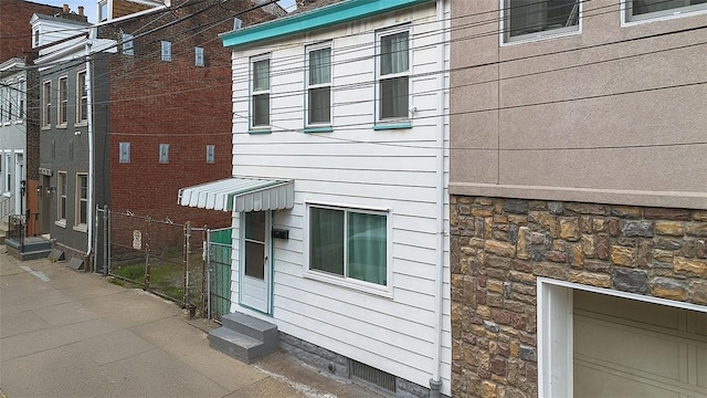 view of side of property with entry steps, stone siding, and fence