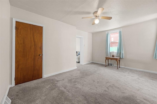 carpeted empty room with ceiling fan, baseboards, and a textured ceiling