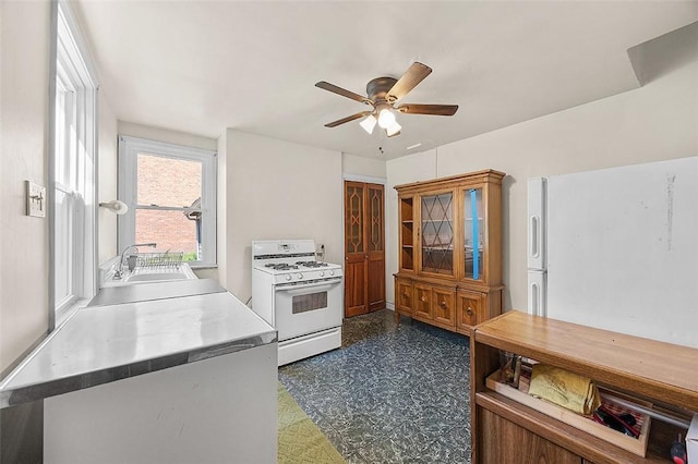 kitchen featuring white range with gas cooktop, a sink, dark floors, a ceiling fan, and light countertops