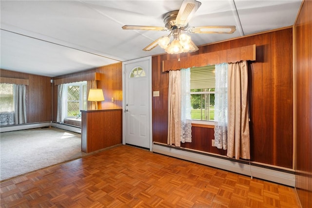 empty room with baseboard heating, ceiling fan, and wood walls
