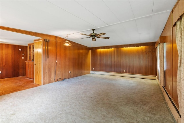 carpeted spare room featuring a baseboard heating unit, wooden walls, a baseboard radiator, and a ceiling fan