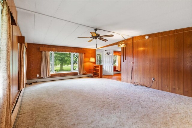 carpeted empty room featuring a baseboard radiator, a ceiling fan, and wooden walls