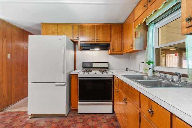 kitchen featuring brick patterned floor, brown cabinets, under cabinet range hood, a sink, and white appliances