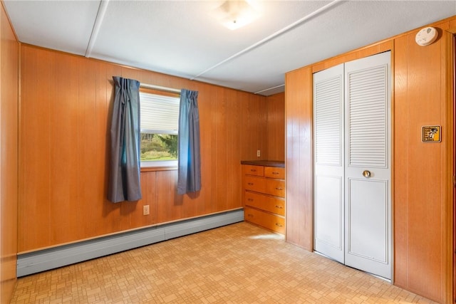 unfurnished bedroom featuring baseboard heating, light floors, wooden walls, and a closet