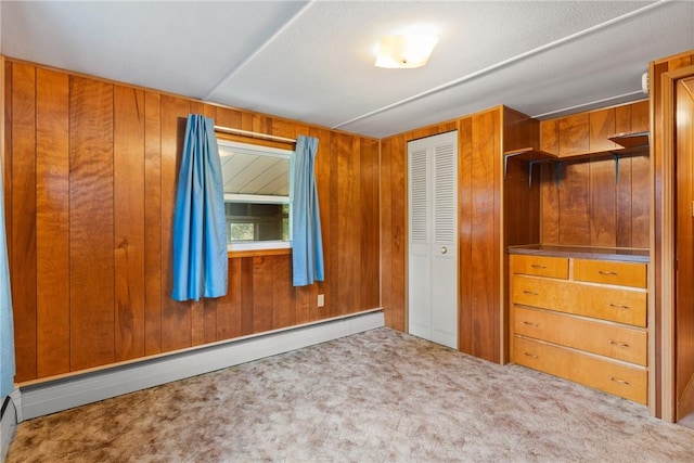 unfurnished bedroom featuring a baseboard radiator, carpet, a closet, and wood walls