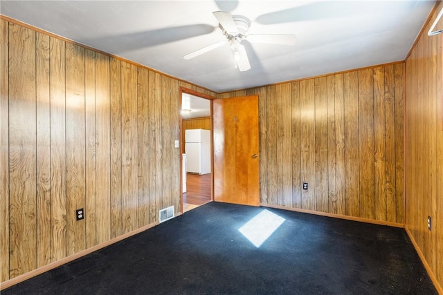 carpeted spare room featuring ceiling fan, wood walls, and visible vents