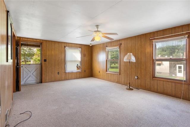 carpeted spare room with a ceiling fan and wood walls