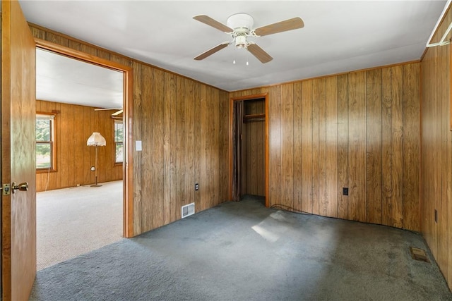 carpeted spare room featuring wooden walls, visible vents, and ceiling fan