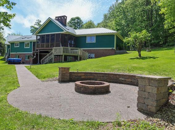 rear view of property featuring an outdoor fire pit, a sunroom, stairs, a lawn, and a chimney