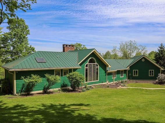view of front of home with a chimney, a front yard, metal roof, and a standing seam roof