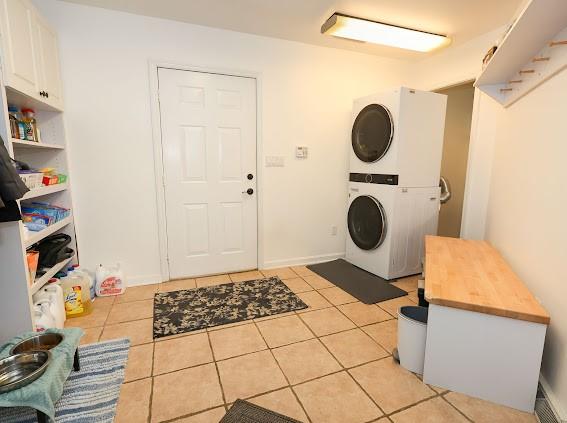 clothes washing area with stacked washer / dryer, light tile patterned floors, cabinet space, and baseboards