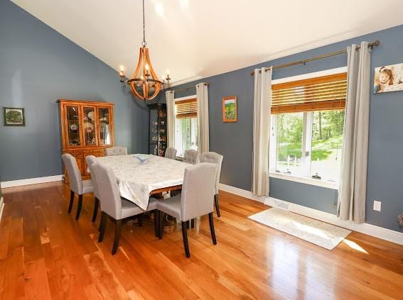 dining room with a chandelier, wood finished floors, baseboards, and high vaulted ceiling