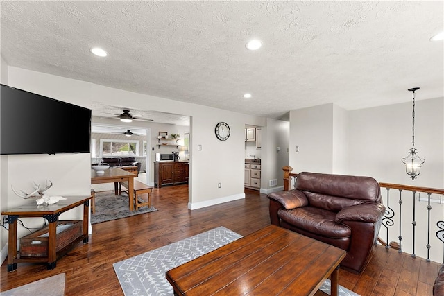 living area with a ceiling fan, a textured ceiling, and dark wood-type flooring