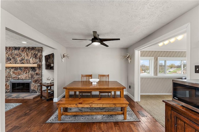 dining area with hardwood / wood-style floors, a ceiling fan, baseboards, a fireplace, and a textured ceiling
