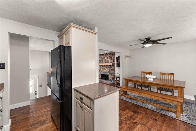 kitchen featuring freestanding refrigerator, a stone fireplace, a ceiling fan, and dark wood-style floors