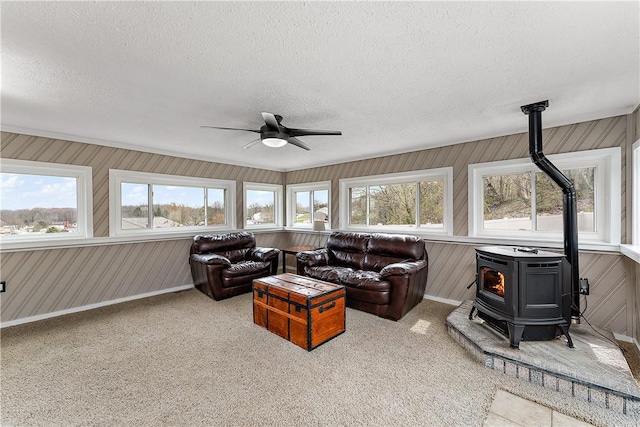 living area featuring a ceiling fan, a wood stove, a textured ceiling, and a healthy amount of sunlight