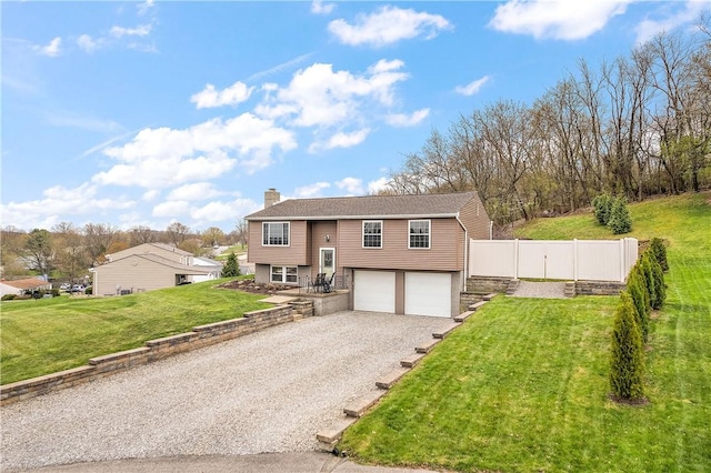 raised ranch with gravel driveway, a chimney, fence, a front lawn, and a garage