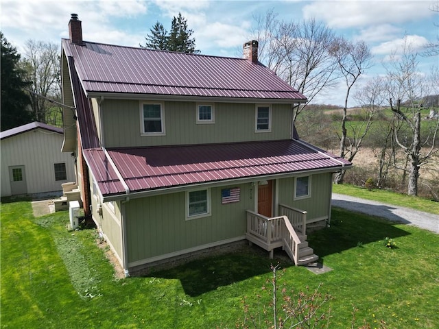 rear view of property featuring a chimney, a lawn, and metal roof