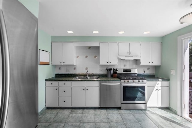 kitchen featuring a sink, tasteful backsplash, dark countertops, under cabinet range hood, and appliances with stainless steel finishes