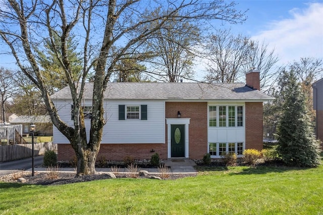 split foyer home featuring a front lawn, a chimney, fence, brick siding, and a shingled roof