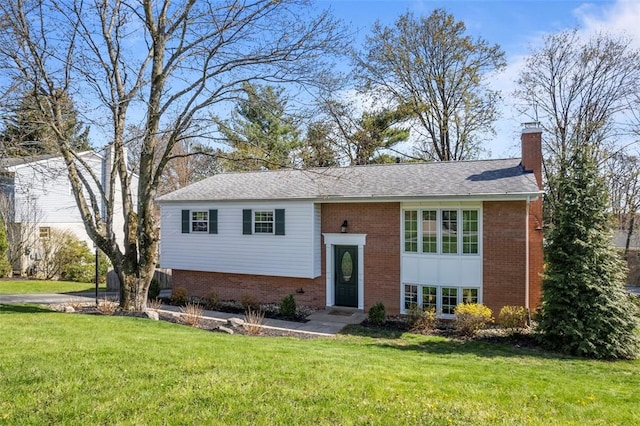 raised ranch featuring a chimney, a front lawn, brick siding, and a shingled roof