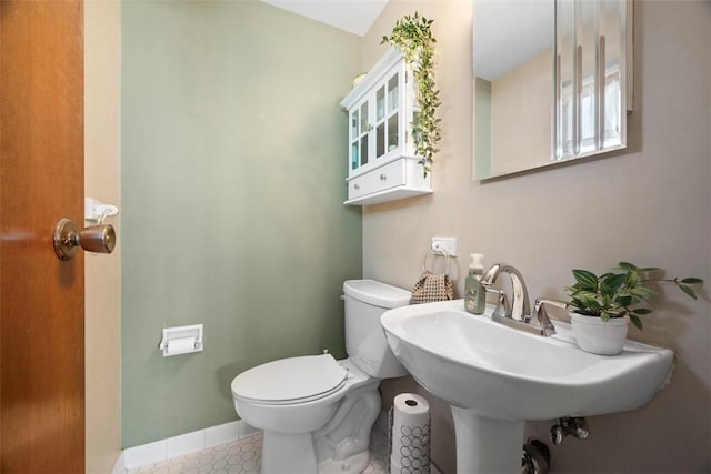 half bathroom featuring toilet, tile patterned flooring, a sink, and baseboards