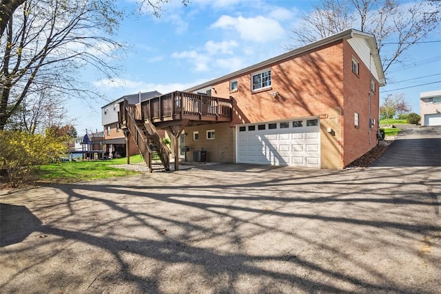 back of property with stairway, a deck, aphalt driveway, central air condition unit, and a garage