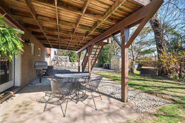 view of patio with outdoor dining space, a grill, an outbuilding, stairs, and a storage unit