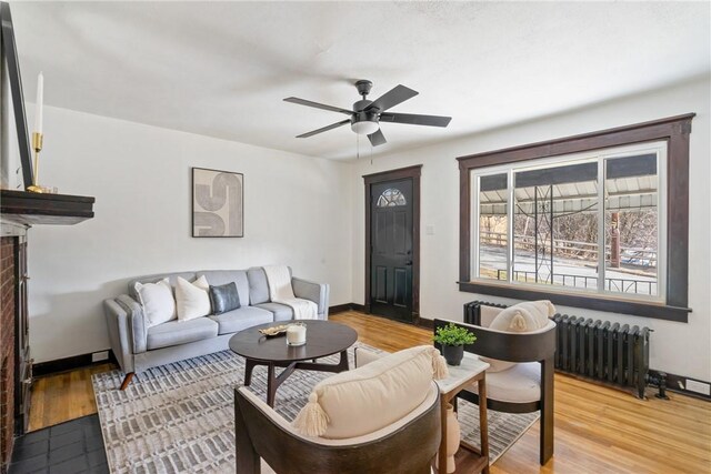 living area with radiator heating unit, a ceiling fan, baseboards, and light wood-type flooring