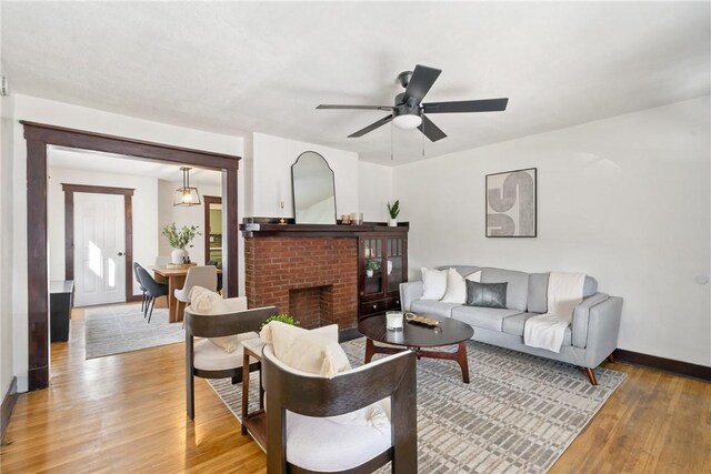 living area with light wood finished floors, a ceiling fan, baseboards, and a brick fireplace