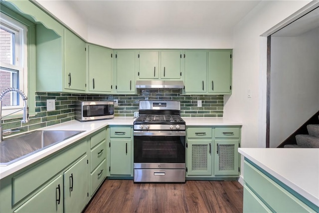 kitchen featuring a sink, light countertops, under cabinet range hood, dark wood-type flooring, and appliances with stainless steel finishes