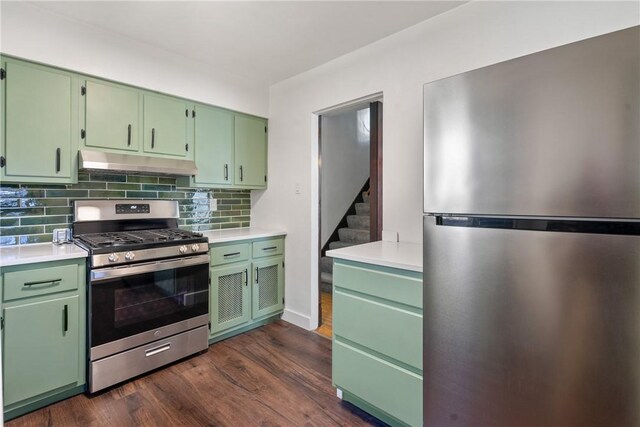 kitchen featuring dark wood finished floors, under cabinet range hood, green cabinets, decorative backsplash, and appliances with stainless steel finishes