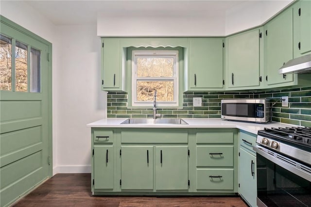 kitchen featuring under cabinet range hood, stainless steel appliances, a sink, green cabinets, and tasteful backsplash