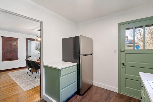 kitchen featuring dark wood-style floors, light countertops, freestanding refrigerator, green cabinets, and baseboards