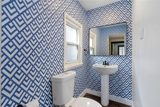 bathroom with wallpapered walls, wood finished floors, toilet, and baseboards