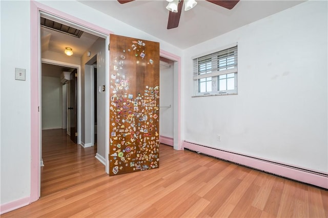 empty room featuring a baseboard heating unit, a ceiling fan, baseboards, and light wood-type flooring