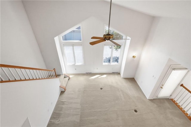 unfurnished living room featuring light colored carpet, stairs, a ceiling fan, and a towering ceiling