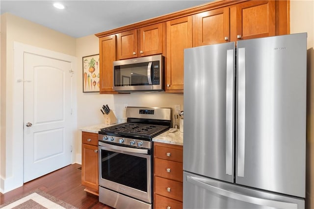 kitchen with light stone countertops, brown cabinets, appliances with stainless steel finishes, and dark wood-style flooring