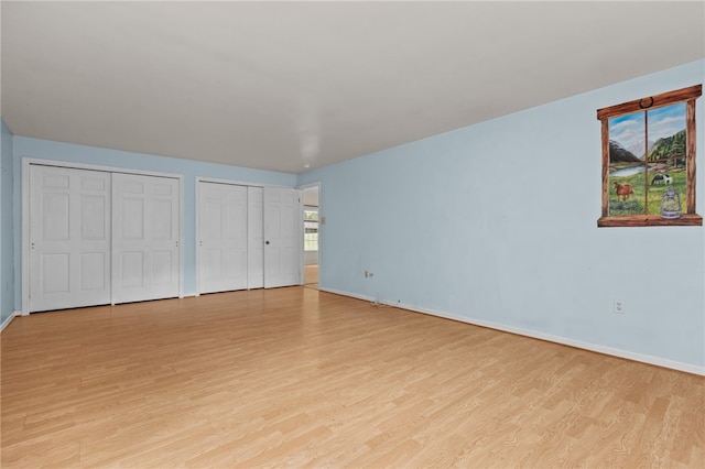 unfurnished bedroom featuring light wood finished floors, multiple closets, and baseboards
