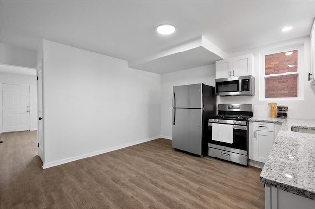 kitchen with white cabinets, stainless steel appliances, wood finished floors, light stone countertops, and baseboards