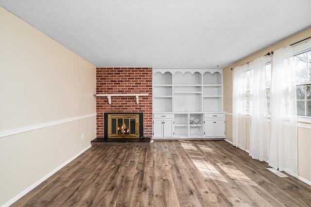 unfurnished living room with dark wood-style floors, a textured ceiling, baseboards, a brick fireplace, and visible vents