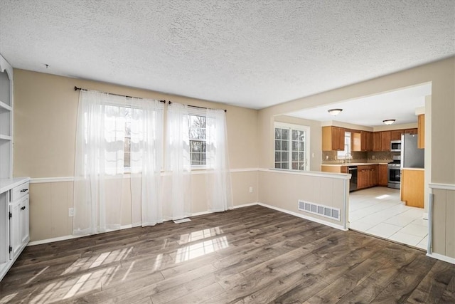 interior space featuring a textured ceiling, wood finished floors, visible vents, and wainscoting