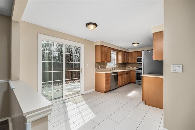 kitchen featuring a sink, brown cabinetry, light countertops, backsplash, and appliances with stainless steel finishes