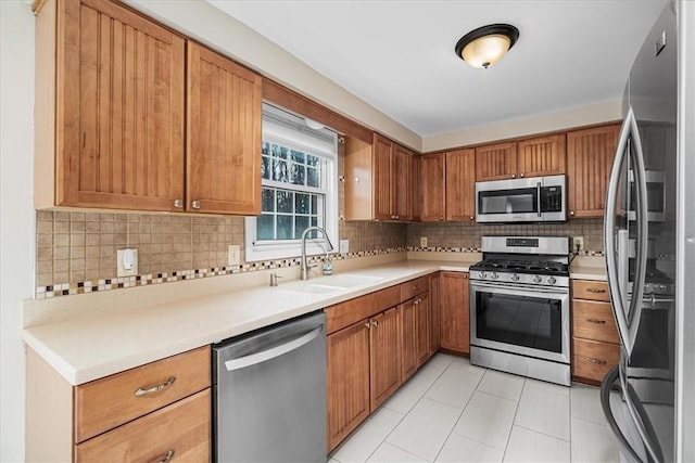 kitchen featuring a sink, brown cabinetry, decorative backsplash, light tile patterned flooring, and appliances with stainless steel finishes
