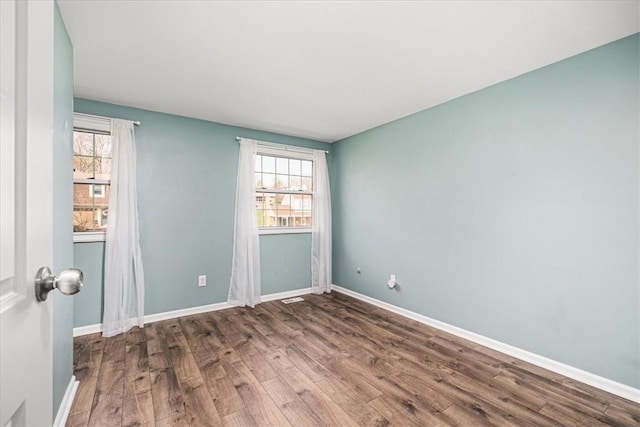 spare room featuring wood finished floors, a wealth of natural light, and baseboards