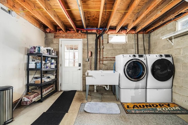 laundry room with concrete block wall, a sink, washer and clothes dryer, and laundry area