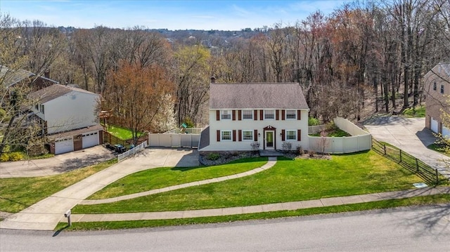 view of front of home featuring a front lawn, a wooded view, concrete driveway, fence, and a garage