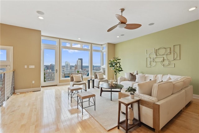 living room with a city view, a ceiling fan, light wood finished floors, and baseboards