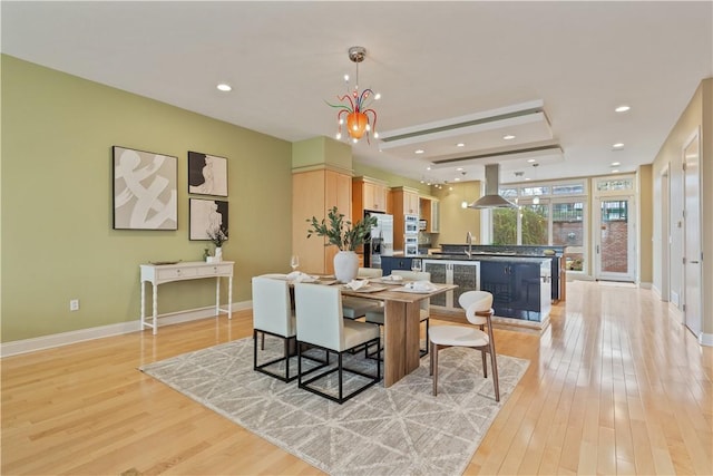 dining room featuring recessed lighting, baseboards, a raised ceiling, and light wood-type flooring